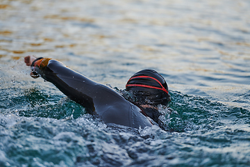 Image showing Triathlon athlete swimming on lake in sunrise wearing wetsuit