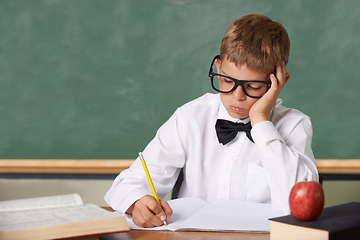 Image showing Frustrated boy child, classroom and writing in books for knowledge, information and studying at academy. Student kid, learning and education with glasses, thinking and stress with dyslexia at school