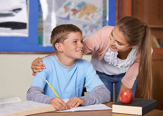 Image showing Happy student, teacher and care in support for education, learning or tutor in classroom at school. Woman, mentor or teaching boy or teen in writing, literature or test for exam or help on class desk