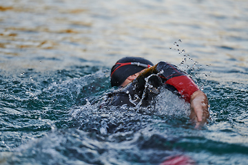 Image showing Triathlon athlete swimming on lake in sunrise wearing wetsuit