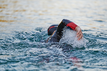 Image showing Triathlon athlete swimming on lake in sunrise wearing wetsuit