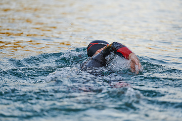 Image showing Triathlon athlete swimming on lake in sunrise wearing wetsuit