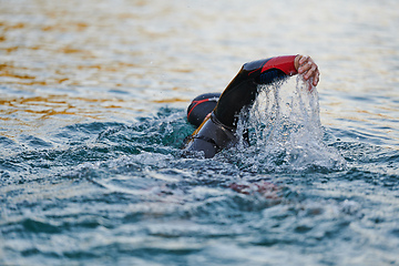 Image showing Triathlon athlete swimming on lake in sunrise wearing wetsuit