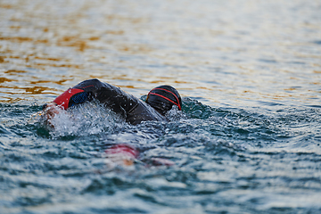 Image showing Triathlon athlete swimming on lake in sunrise wearing wetsuit