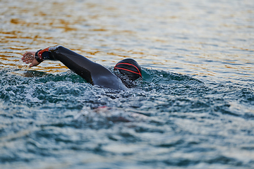 Image showing Triathlon athlete swimming on lake in sunrise wearing wetsuit