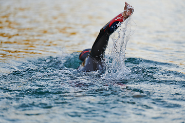 Image showing Triathlon athlete swimming on lake in sunrise wearing wetsuit