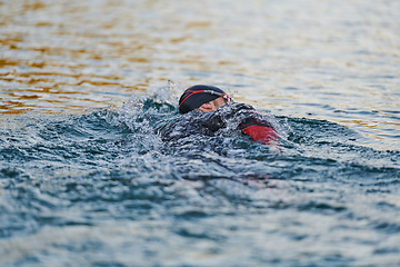 Image showing Triathlon athlete swimming on lake in sunrise wearing wetsuit