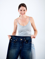 Image showing Jeans, weight loss and portrait of woman with change in size on white background in studio. Body, transformation and person with journey in diet, fitness and healthy results with large denim pants