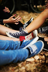 Image showing Sneakers, legs and friends on the ground outdoor in autumn together to relax or chill closeup. Fashion, style and casual with the shoes of a group of people sitting on leaves during the fall season