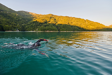 Image showing Triathlon athlete swimming on lake in sunrise wearing wetsuit