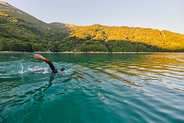 Image showing Triathlon athlete swimming on lake in sunrise wearing wetsuit