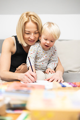 Image showing Caring young Caucasian mother and small son drawing painting in notebook at home together. Loving mom or nanny having fun learning and playing with her little 1,5 year old infant baby boy child.