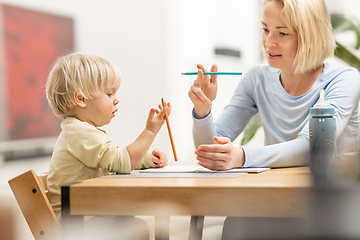 Image showing Caring young Caucasian mother and small son drawing painting in notebook at home together. Loving mom or nanny having fun learning and playing with her little 1,5 year old infant baby boy child.