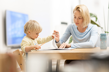 Image showing Caring young Caucasian mother and small son drawing painting in notebook at home together. Loving mom or nanny having fun learning and playing with her little 1,5 year old infant baby boy child.