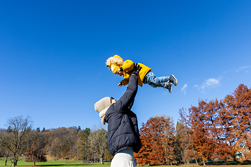 Image showing More, more,...mum, that's fun. Happy young mother throws her cute little baby boy up in the air. Mother's Day, Mather and her son baby boy playing and hugging outdoors in nature in fall.