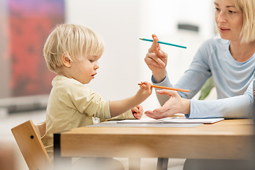 Image showing Caring young Caucasian mother and small son drawing painting in notebook at home together. Loving mom or nanny having fun learning and playing with her little 1,5 year old infant baby boy child.