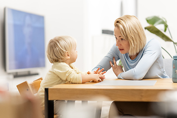 Image showing Caring young Caucasian mother and small son drawing painting in notebook at home together. Loving mom or nanny having fun learning and playing with her little 1,5 year old infant baby boy child.