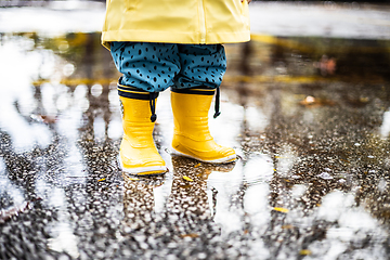 Image showing Small infant boy wearing yellow rubber boots and yellow waterproof raincoat standing in puddle on a overcast rainy day. Child in the rain.