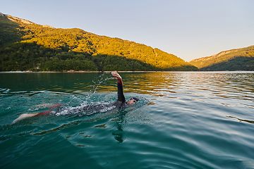 Image showing Triathlon athlete swimming on lake in sunrise wearing wetsuit