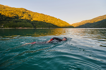 Image showing Triathlon athlete swimming on lake in sunrise wearing wetsuit