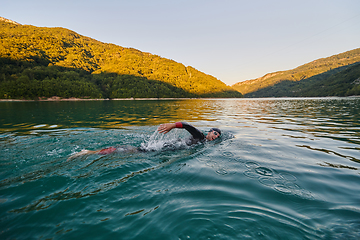 Image showing Triathlon athlete swimming on lake in sunrise wearing wetsuit