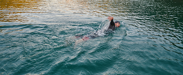 Image showing A professional triathlete trains with unwavering dedication for an upcoming competition at a lake, emanating a sense of athleticism and profound commitment to excellence.