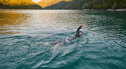 Image showing Triathlon athlete swimming on lake in sunrise wearing wetsuit