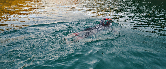 Image showing A professional triathlete trains with unwavering dedication for an upcoming competition at a lake, emanating a sense of athleticism and profound commitment to excellence.