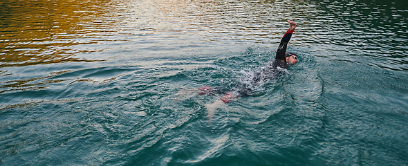 Image showing A professional triathlete trains with unwavering dedication for an upcoming competition at a lake, emanating a sense of athleticism and profound commitment to excellence.