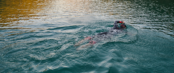 Image showing A professional triathlete trains with unwavering dedication for an upcoming competition at a lake, emanating a sense of athleticism and profound commitment to excellence.