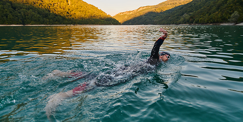 Image showing Triathlon athlete swimming on lake in sunrise wearing wetsuit