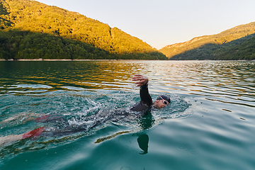 Image showing Triathlon athlete swimming on lake in sunrise wearing wetsuit