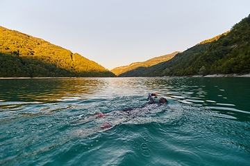 Image showing Triathlon athlete swimming on lake in sunrise wearing wetsuit