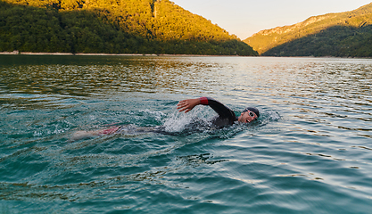 Image showing Triathlon athlete swimming on lake in sunrise wearing wetsuit