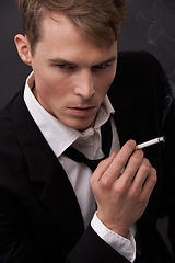 Image showing Face, thinking and a man smoking a cigarette in studio on a dark background for tobacco addiction. Nicotine, habit and unhealthy with a young person in a suit, taking a break from business to smoke