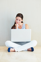 Image showing Woman, laptop and thinking for idea, decision or choice sitting against a wall at home. Female person freelancer in wonder, thought or planning for online research or communication on floor at house