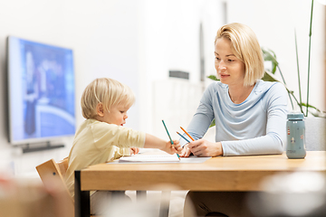 Image showing Caring young Caucasian mother and small son drawing painting in notebook at home together. Loving mom or nanny having fun learning and playing with her little 1,5 year old infant baby boy child.