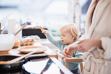 Image showing Mother and little toddler baby boy making pancakes for breakfast together in domestic kitchen. Family, lifestyle, domestic life, food, healthy eating and people concept.