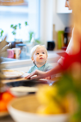 Image showing Mother and little toddler baby boy making pancakes for breakfast together in domestic kitchen. Family, lifestyle, domestic life, food, healthy eating and people concept.