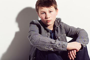 Image showing Serious, boy and portrait of teenager with fashion in studio, white background or mockup. Child, sitting and relax in cool style and clothes with confidence, pride and hipster personality in space