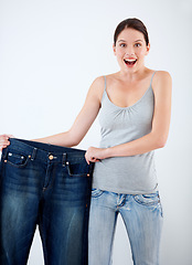 Image showing Surprise, weight loss and woman with jeans, change in size and white background in studio. Wow, shocked and portrait of person with crazy reaction to transformation in fitness or large denim pants