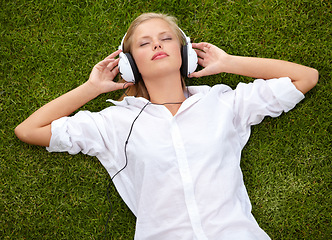 Image showing Woman, relax on grass and listening to music with audio streaming service and mental health in park or garden. Young student sleeping or dream of electronics with headphones on lawn or floor above