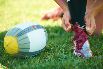 Image showing Rugby, ball and hands with shoes of person on field for training, practice and challenge. Health, start and games with closeup of sports athlete tying laces on outdoor pitch for stadium and fitness