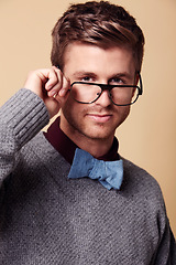 Image showing Portrait, glasses and bowtie for fashion with a man in studio on a tan background for vision or style. Face, eyewear and accessories with a confident young geek or nerd in a casual clothing outfit