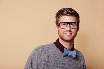 Image showing Portrait, glasses and bowtie for fashion with a man on space in studio for vision or trendy style. Face, smile and eyewear with a confident young model on a tan background in a casual clothing outfit