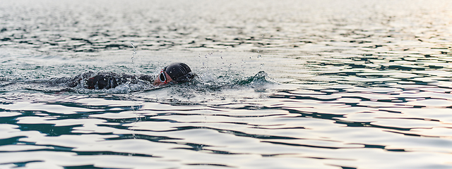 Image showing A professional triathlete trains with unwavering dedication for an upcoming competition at a lake, emanating a sense of athleticism and profound commitment to excellence.