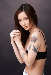 Image showing Asian woman, tattoo and serious portrait in studio, dark background and show art on skin. Japanese, model and unique ink on body with lady in jeans, shorts and underwear with style and pride