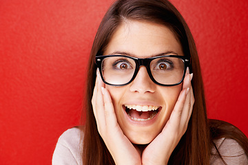 Image showing Portrait, glasses and face of happy woman in surprise for winning, prize or good news against a red studio background. Young friendly or excited female person smile in shock, alert or wow on mockup