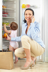 Image showing Phone call, grocery and mother in home with kid at fridge in kitchen, conversation and smile. Smartphone, happy mom and fruit, orange and family packing food in refrigerator with child in connection