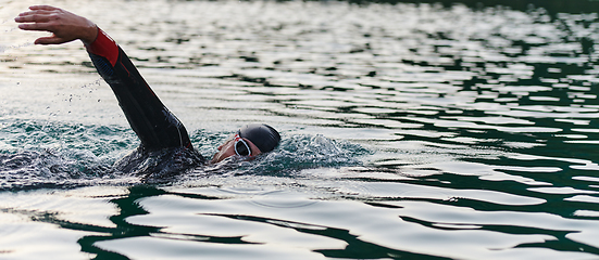 Image showing A professional triathlete trains with unwavering dedication for an upcoming competition at a lake, emanating a sense of athleticism and profound commitment to excellence.